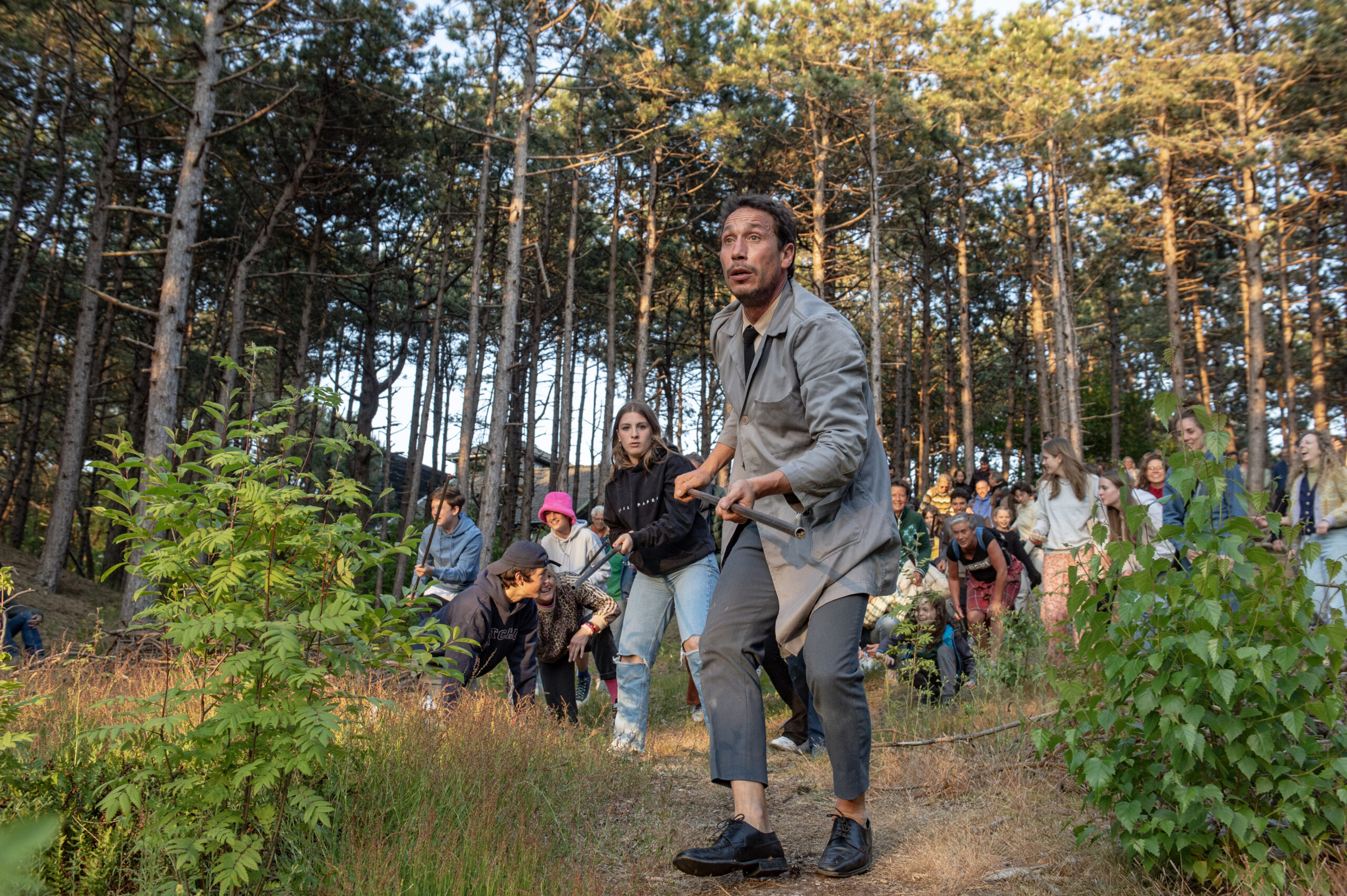 De in grijs geklede geluidskunstenaar Joan Catala loopt met een grote groep publiek door het bos op weg naar zijn voorstelling Idiofona tijdens Oerol 2023.