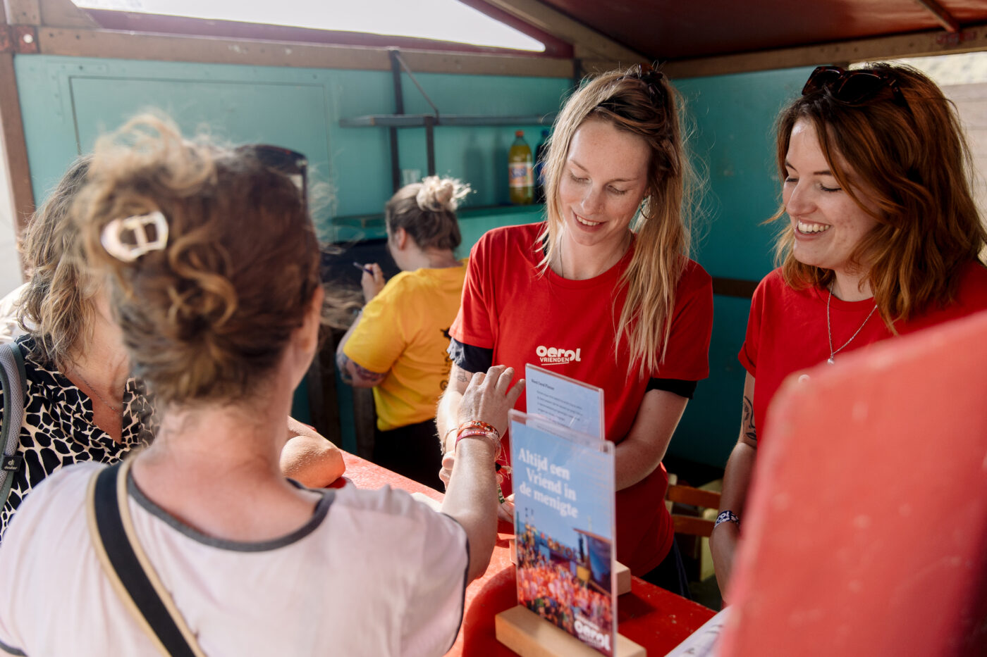 Twee vrijwilligers doen een vriendenbandje om bij een Vriend van Oerol, Oerol 2023