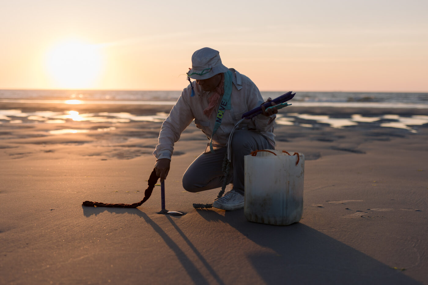 Een man verzamelt materiaal op het Terschellinger strand, een voorstellingsbeeld expeditie voorstelling Interspecies Supermarket van De Onkruidenier tijdens Oerol 2023.