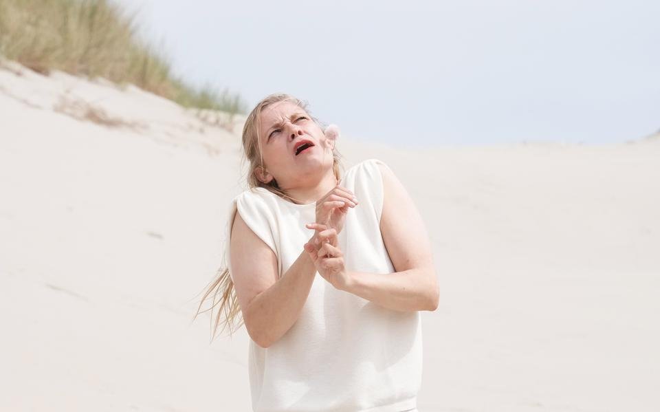 Tegen de achtergrond van witte duinen vertrekt Actrice Eva Meijering haar gezicht om de pijn en het ongemak van onophoudelijke jeuk te tonen, een beeld uit de theatervoorstelling Sâlt van de Friese theatergroep Tryater gespeeld op Oerol 2023.