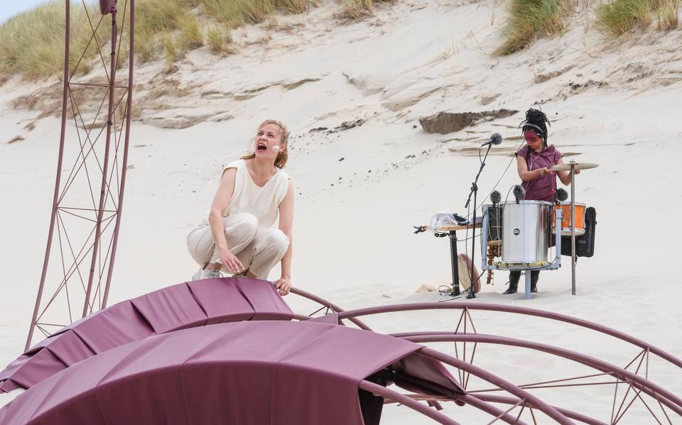 Actrice Eva Meijering in de roodstalen contstructie dat als decor dient voor haar voorstelling Sâlt van Tryater, met op de achtergrond live muzikant Michelle Samba, gespeeld tijdens Oerol 2023.