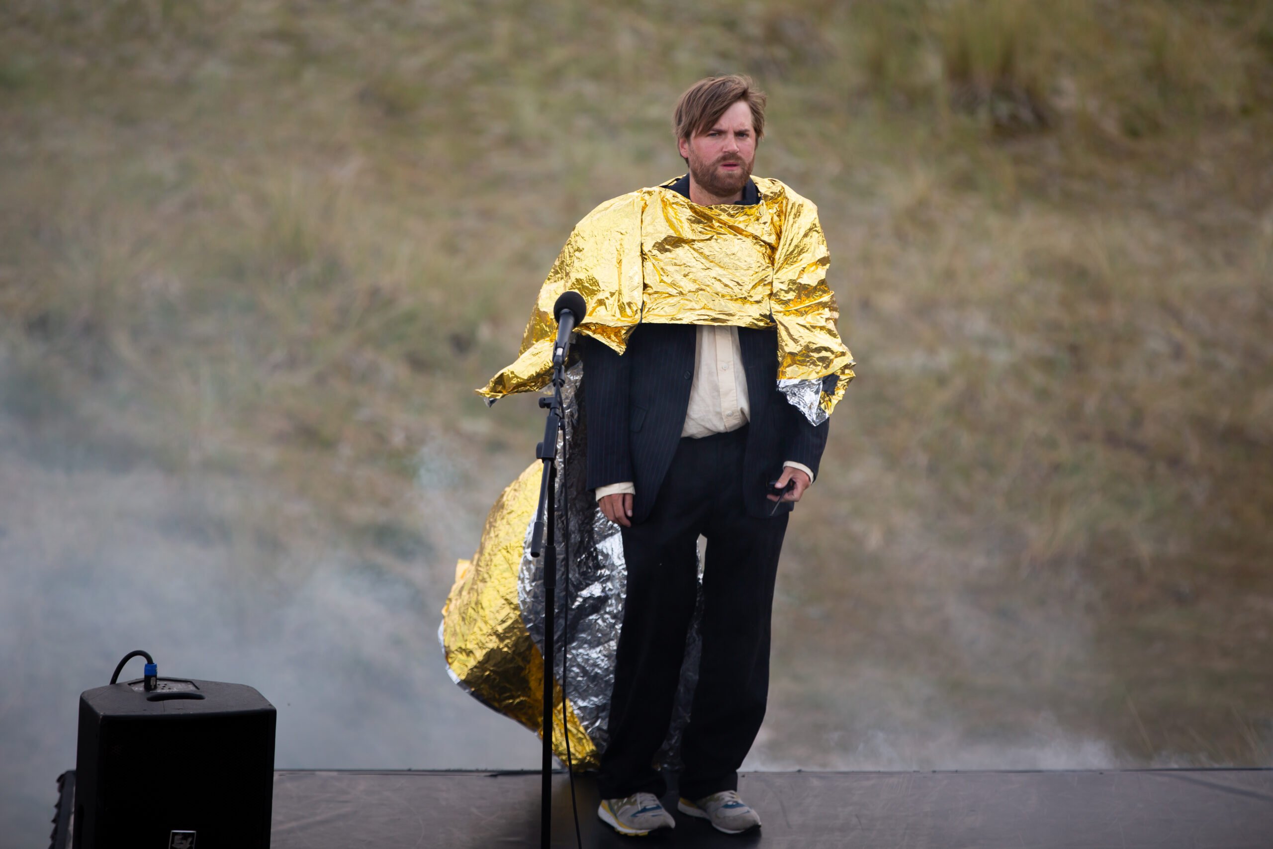 Een jonge acteur staat in een ouderwets zwart pak op het podium met goud met zilverkleurige folie als een cape om hem heen gewikkeld tijdens De voorstelling met misschien wel de langste opkomst ooit van Elias de Bruyne (Atelier 2022)