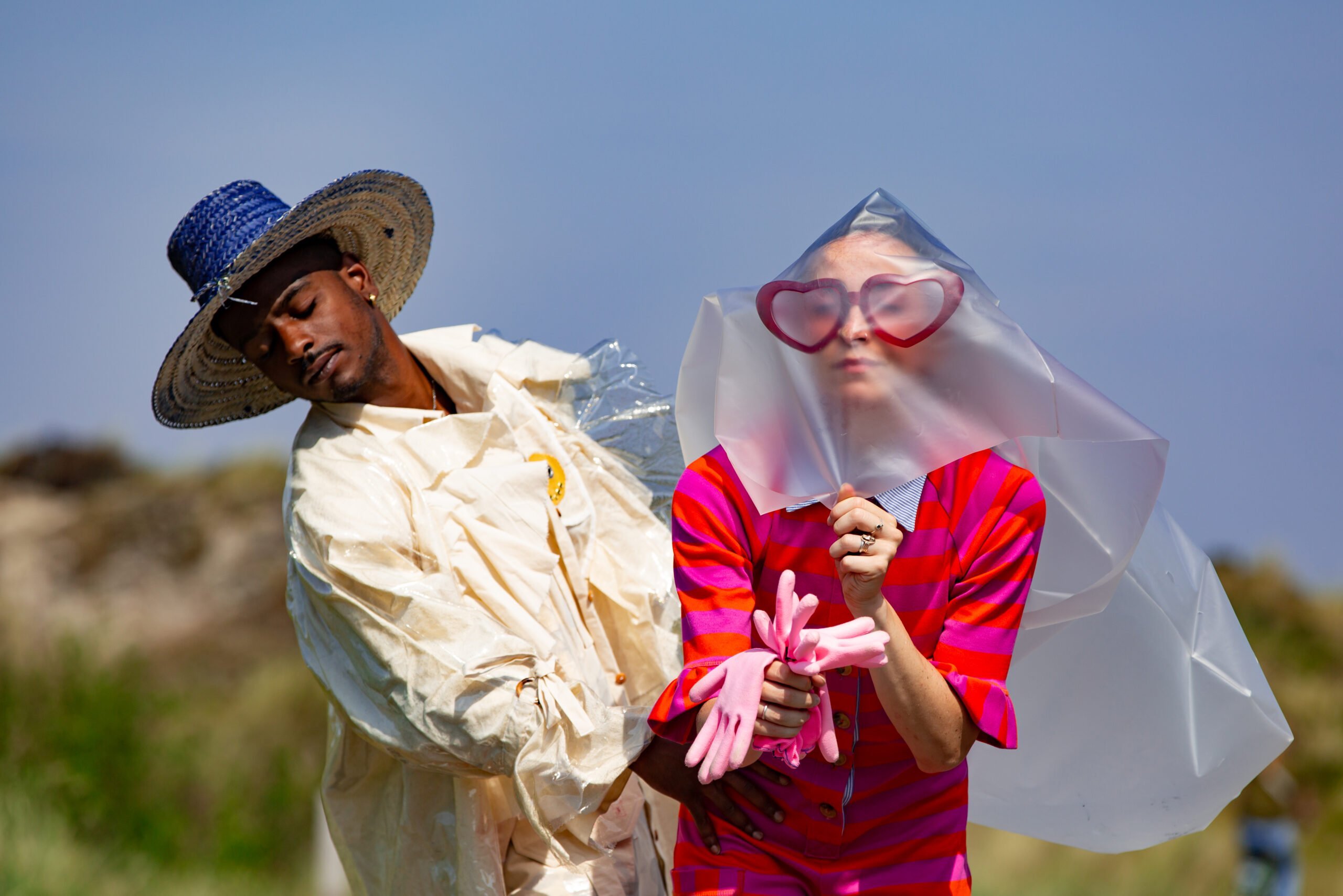 Twee mensen dansen in de natuur. Hij in een wit pak vol strikken met een blauwe strooien, zij in het roze-rood gestreept met een grote rode hartjesbril, roze rubberen handschoenen en een sluier van melkglas plastic die over haar gezicht naar achter wappert. Een beeld uit Hurry slowly, but hurry van Lunatics and Poets
