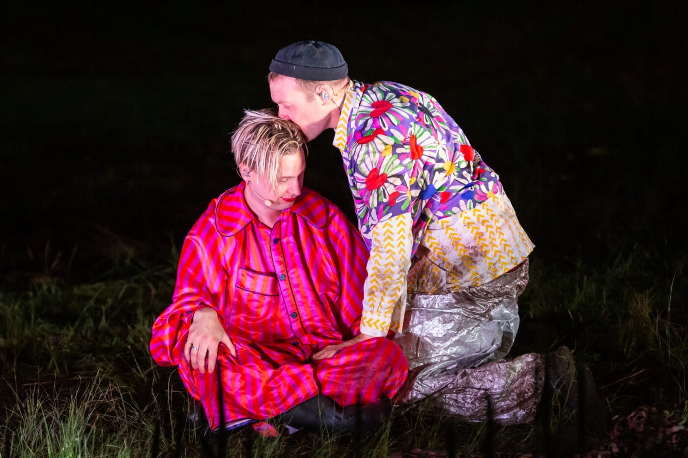 twee mensen in felgekleurde kleding waarvan de een de ander een kus op het hoofd geeft in de theatervoorstelling The world is as you are, een experimenteel theaterconcert van Maas theater en dans x REINDIER gespeeld op Oerol 2022.