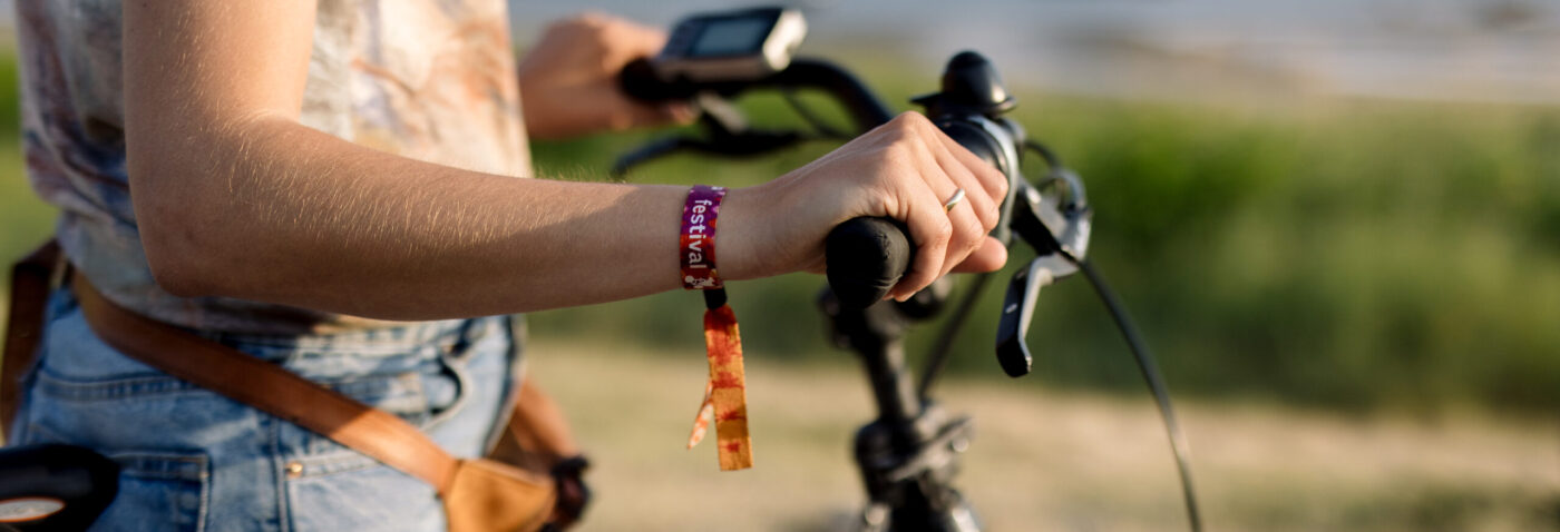 Vrouw op de fiets met een festivalbandje voor Oerol 2023.