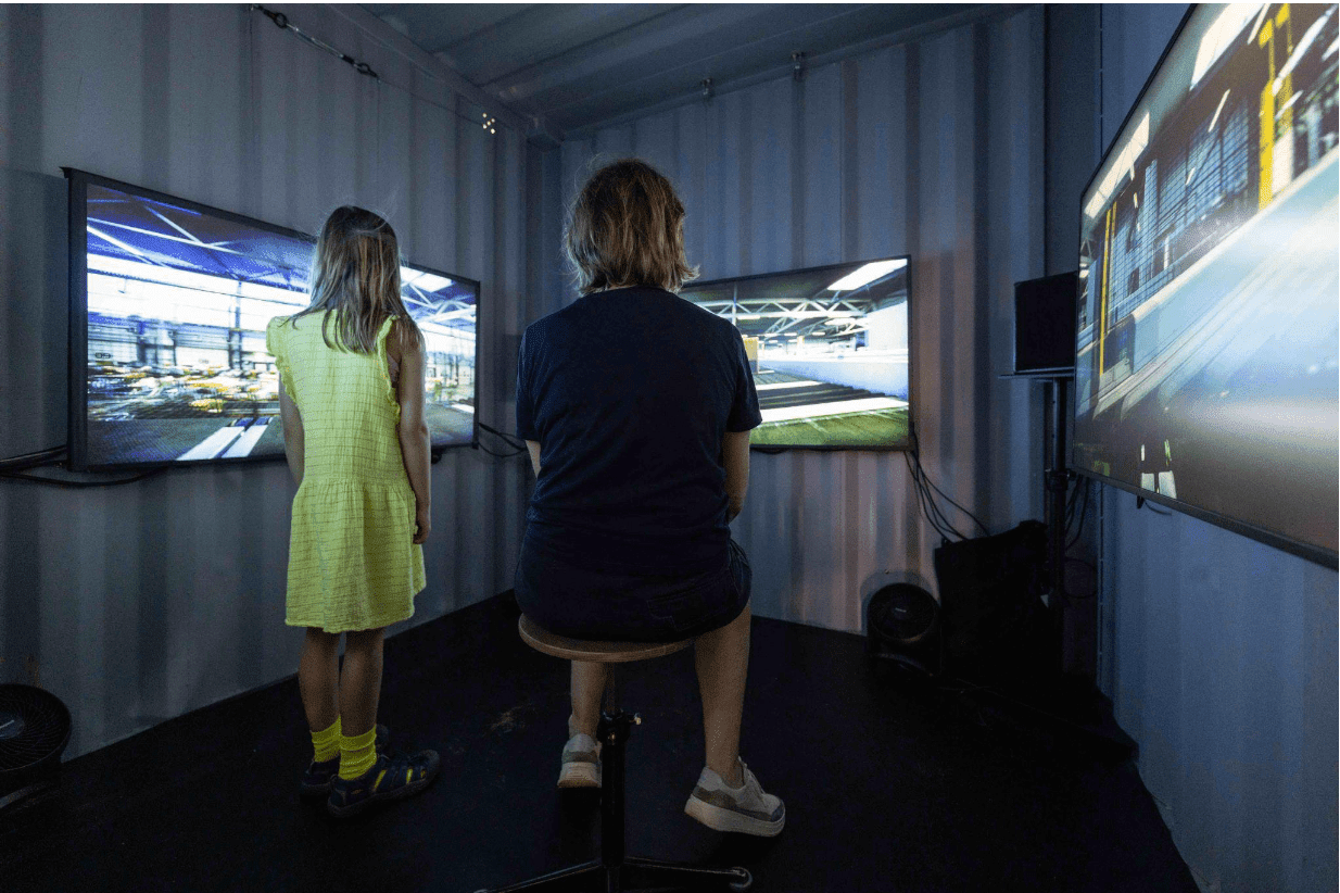 een jongen en een klein meisje kijken in een container naar 3 grote tv-schermen