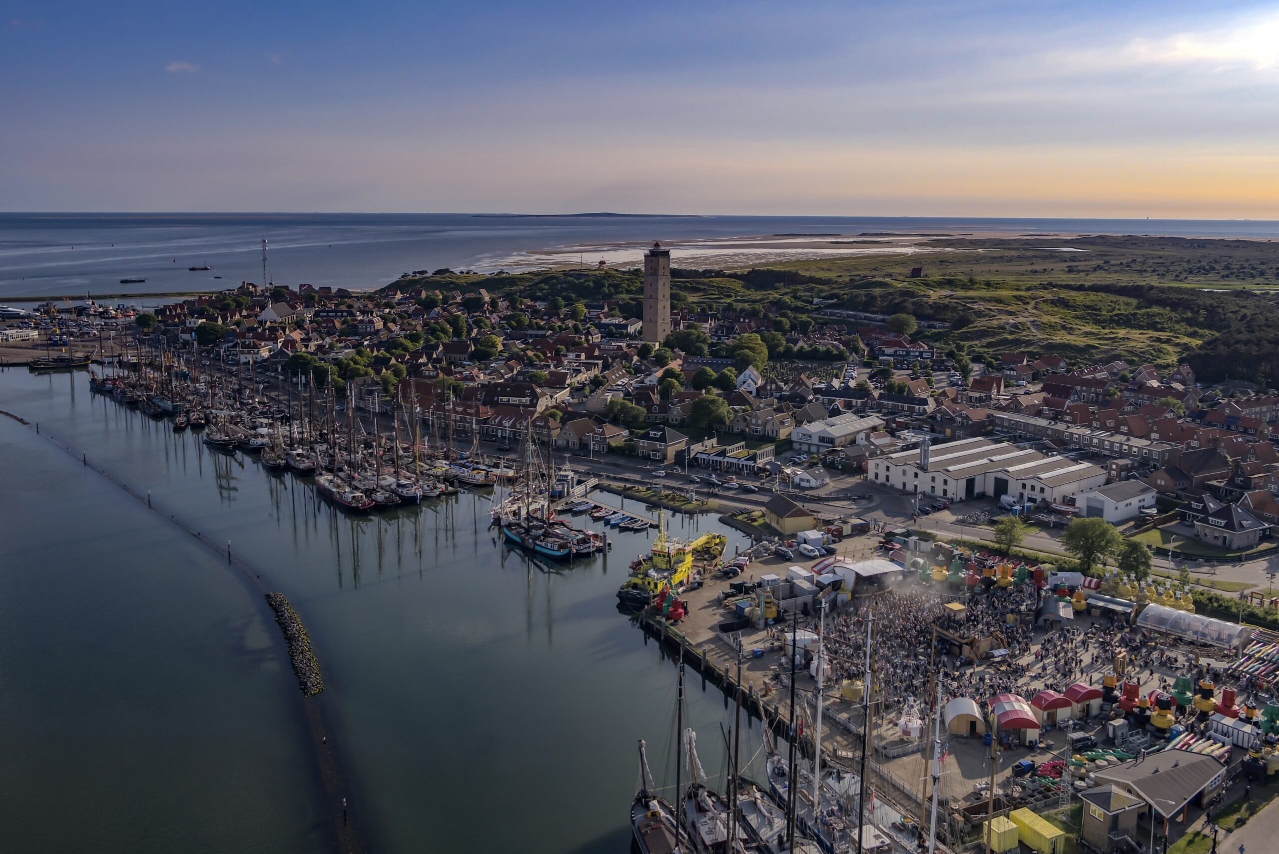 Een droneshot van West-Terschelling tijdens Oerol waarop het dorp te zien is, de jachthaven, vuurtoren de Brandaris en voormalig festivalterrein de Betonning.