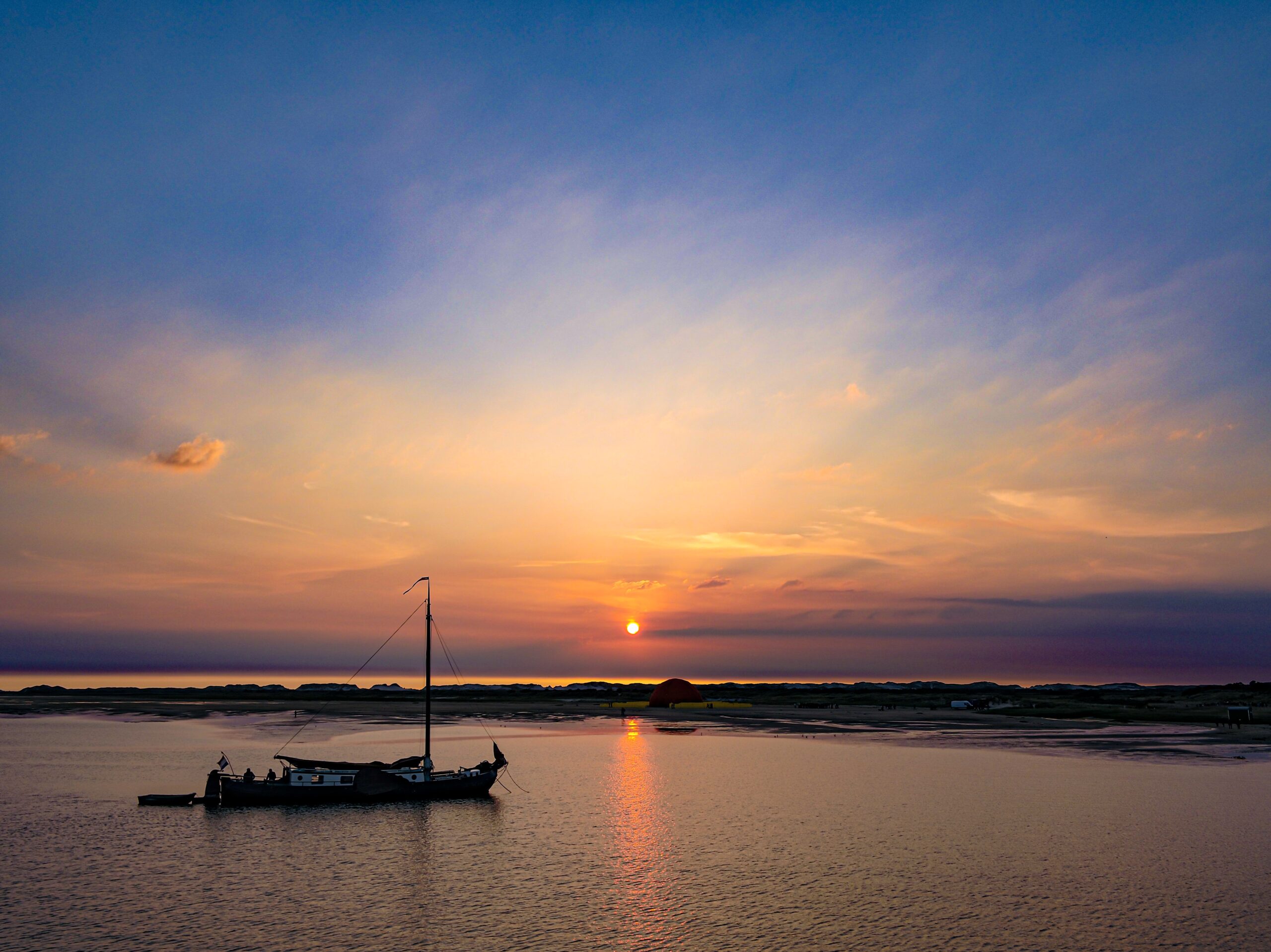 Schip drooggevallen op het wad met op de achtergrond een felrode zonsondergang boven het rood-gele decor van het Nieuw Utrechts Toneel