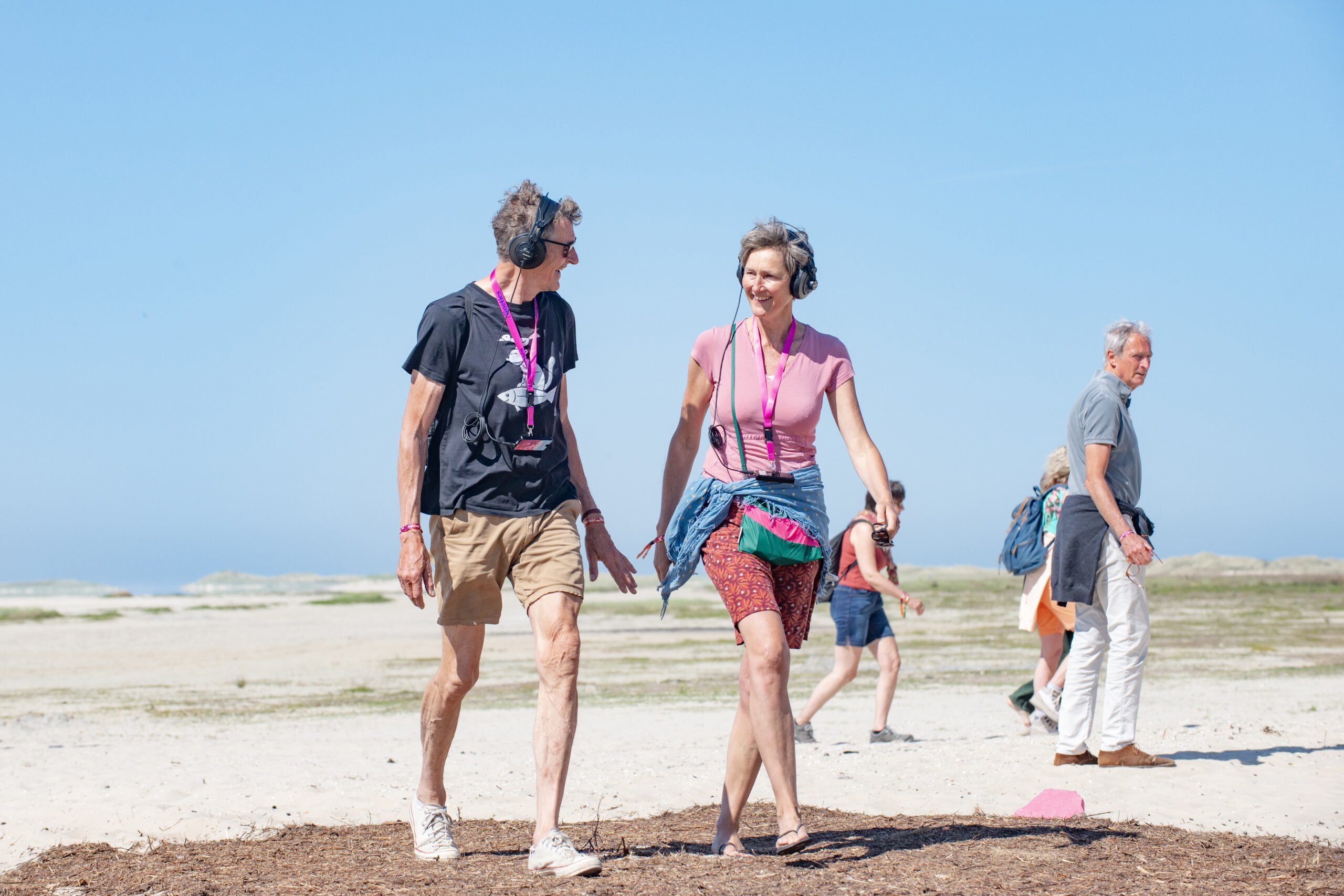 Twee mensen lopen een audiowandeling met koptelefoon op hun hoofd, tijdens een expeditie op Oerol 2023