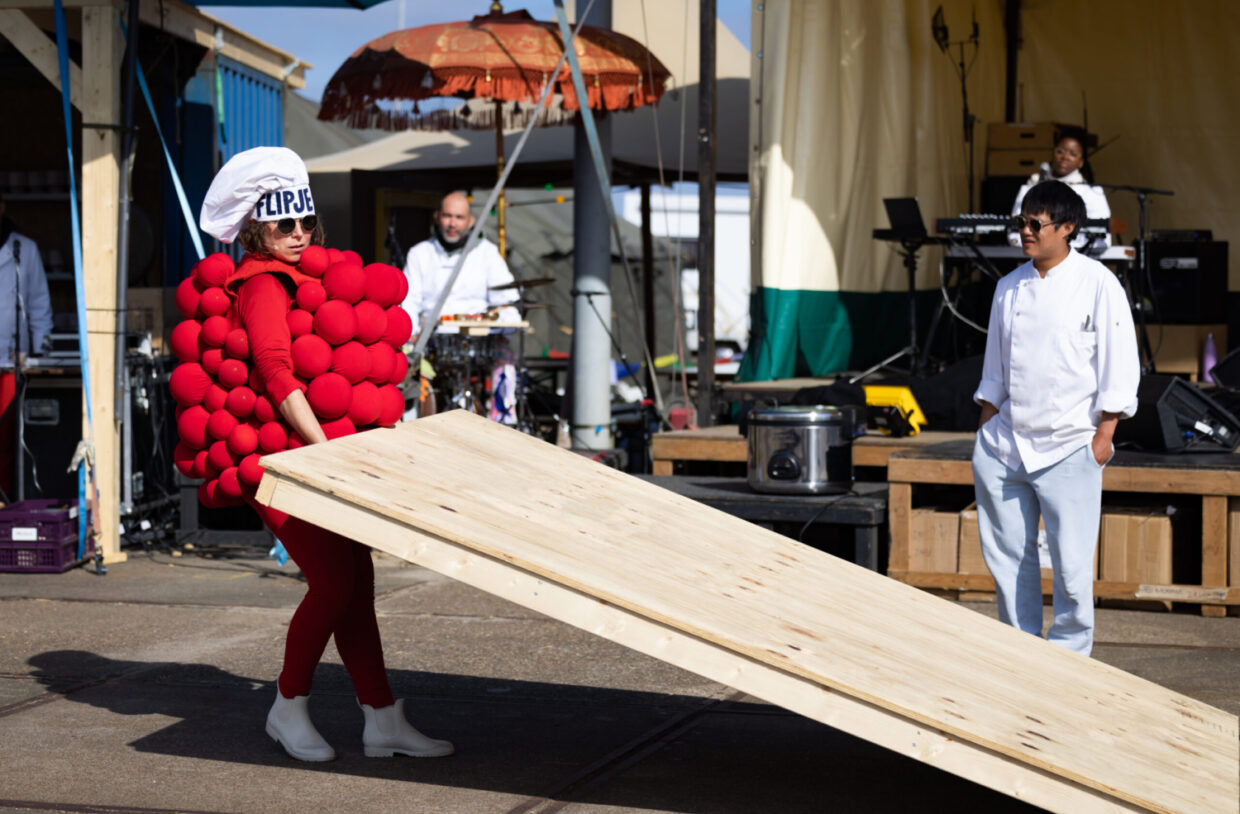 Vrouw in Flipje kostuum sjouwt met een tafel, voorstellingsbeeld uit Wereld van Wie van theatergroep Veenfabriek gespeeld tijdens Oerol 2023