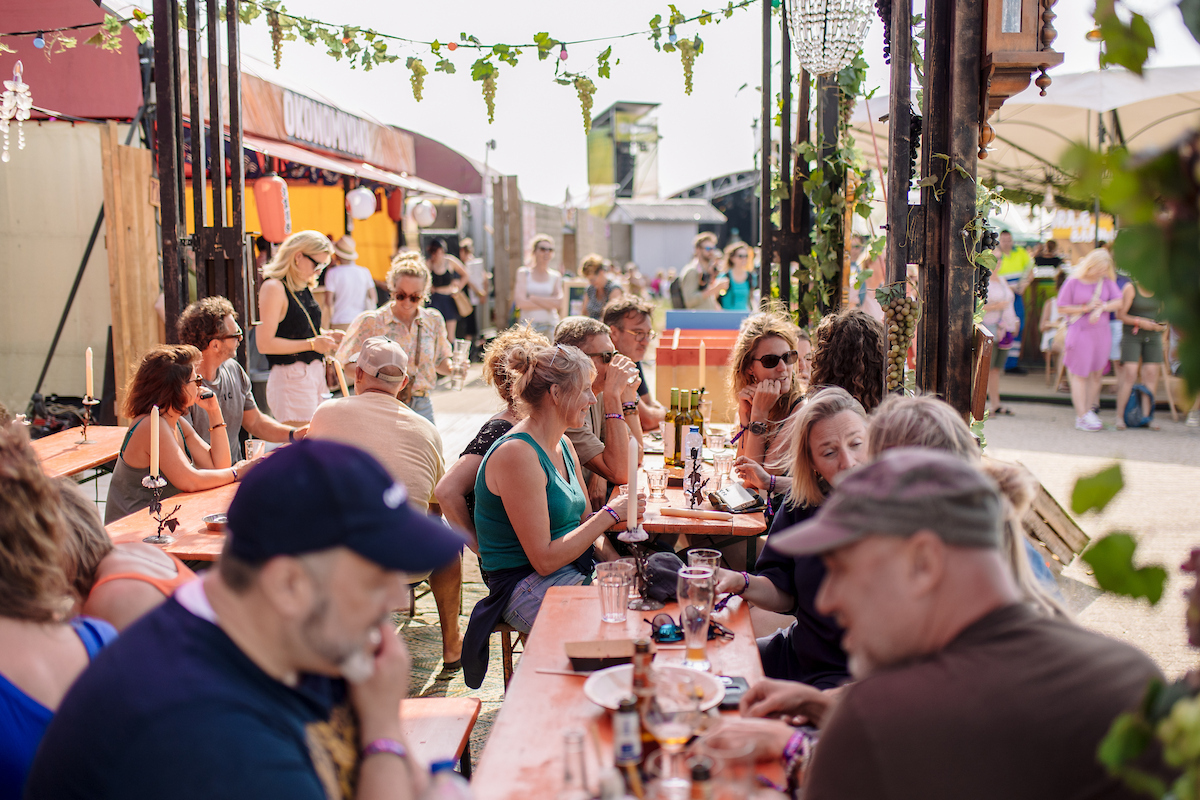 een lange rij tafels met glazen en eten erop en verschillende mensen eraan op festivalhart de Deining.